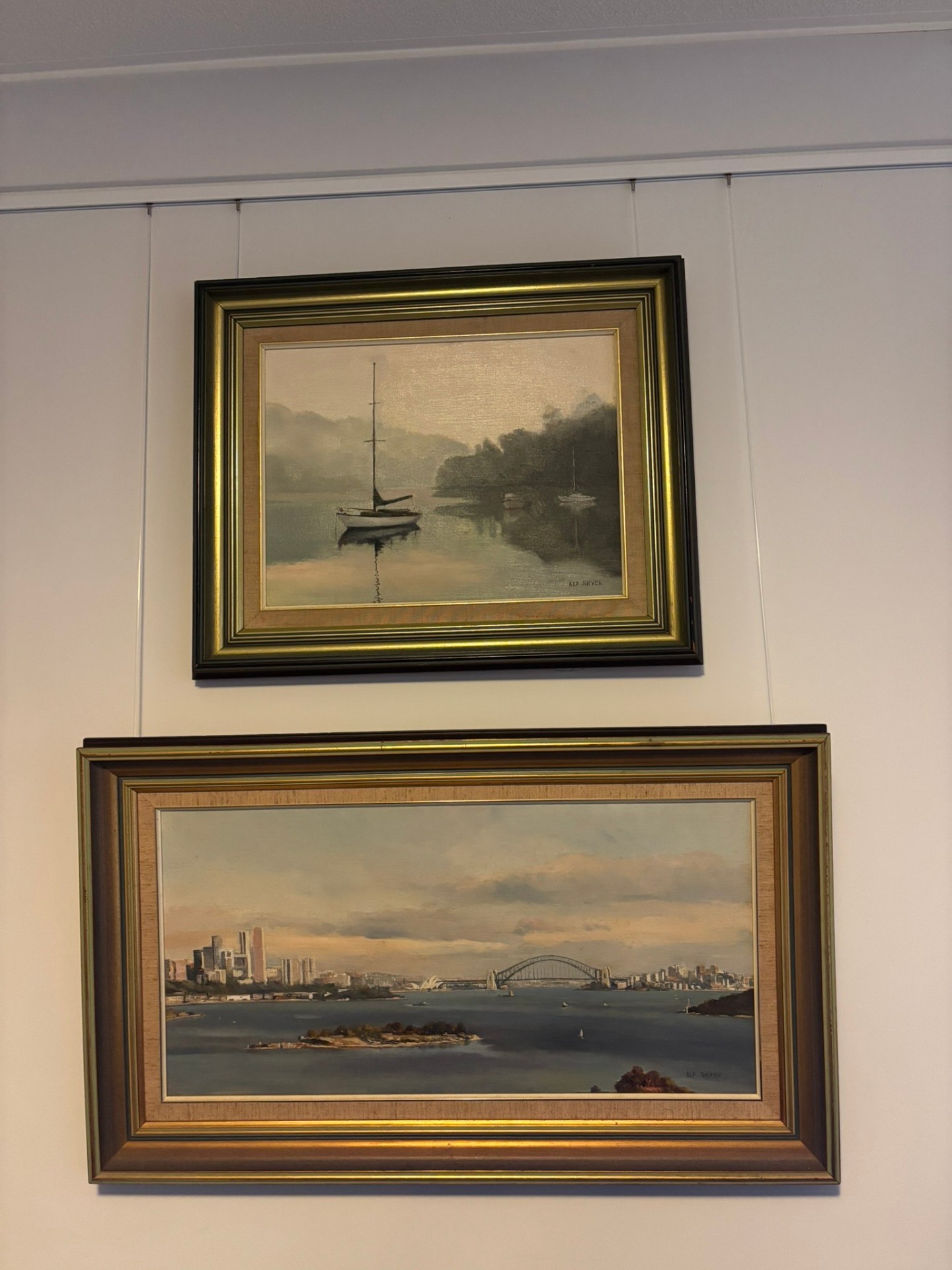 Two framed harbour paintings hung on wires