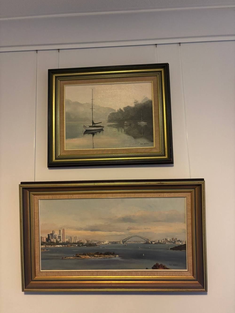 Two framed paintings suspended from a white picture rail