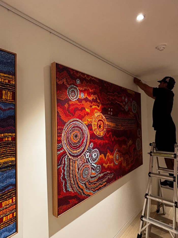 Installer hanging large indigenous artwork on a rail system