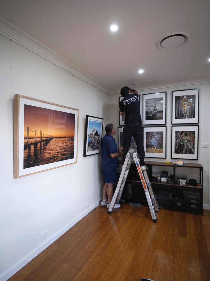 Installers hanging a gallery wall of framed photography
